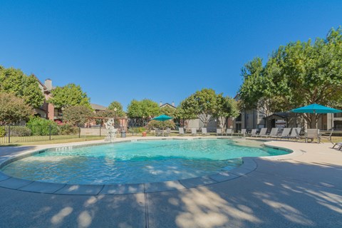 a swimming pool with umbrellas and buildings in the background at Fountains of Denton in Denton, TX