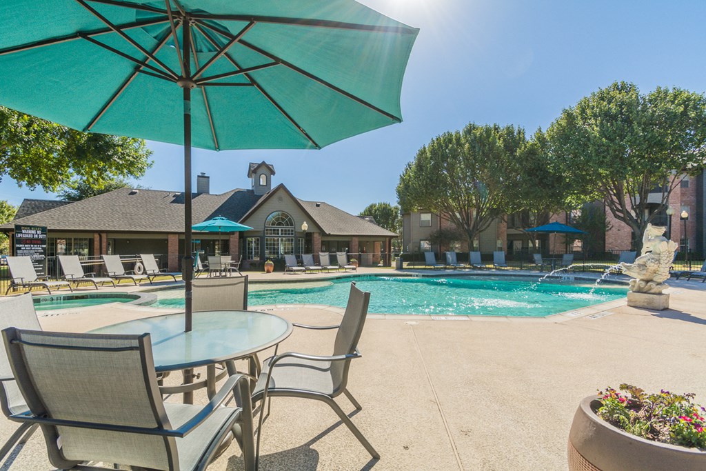 pool and patio with chairs and umbrellas at Fountains of Denton in Denton, TX
