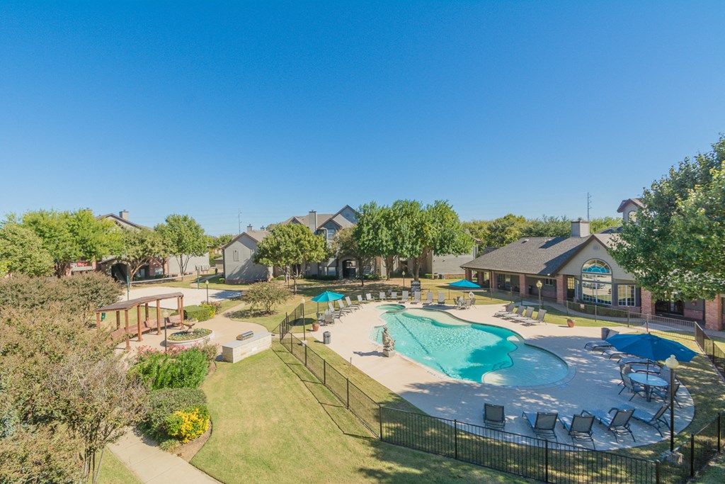 an aerial view of a swimming pool with patio furniture and resort style apartment buildings at Fountains of Denton in Denton, TX