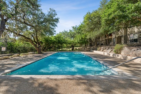 A rectangular pool surrounded by trees and a fence.