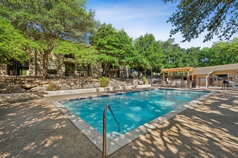 A pool surrounded by trees and a building in the background.
