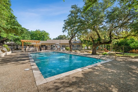 A swimming pool surrounded by trees and a building in the background.