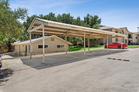 A parking lot with a covered parking structure and a red car parked in front of a building.