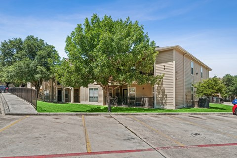 A parking lot in front of a building with a tree in front of the building.