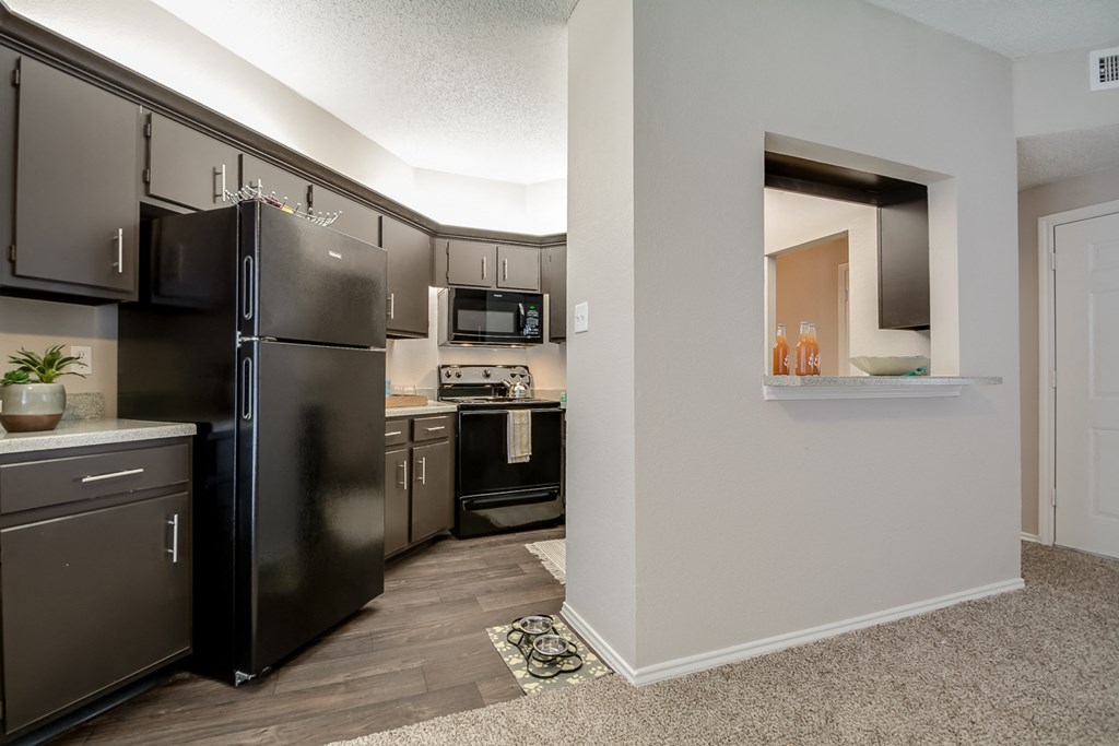 A kitchen with a black refrigerator and a white wall.