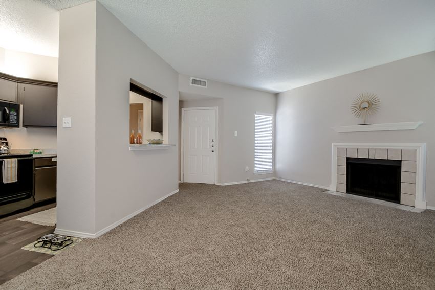 an empty living room with a fireplace and a kitchen