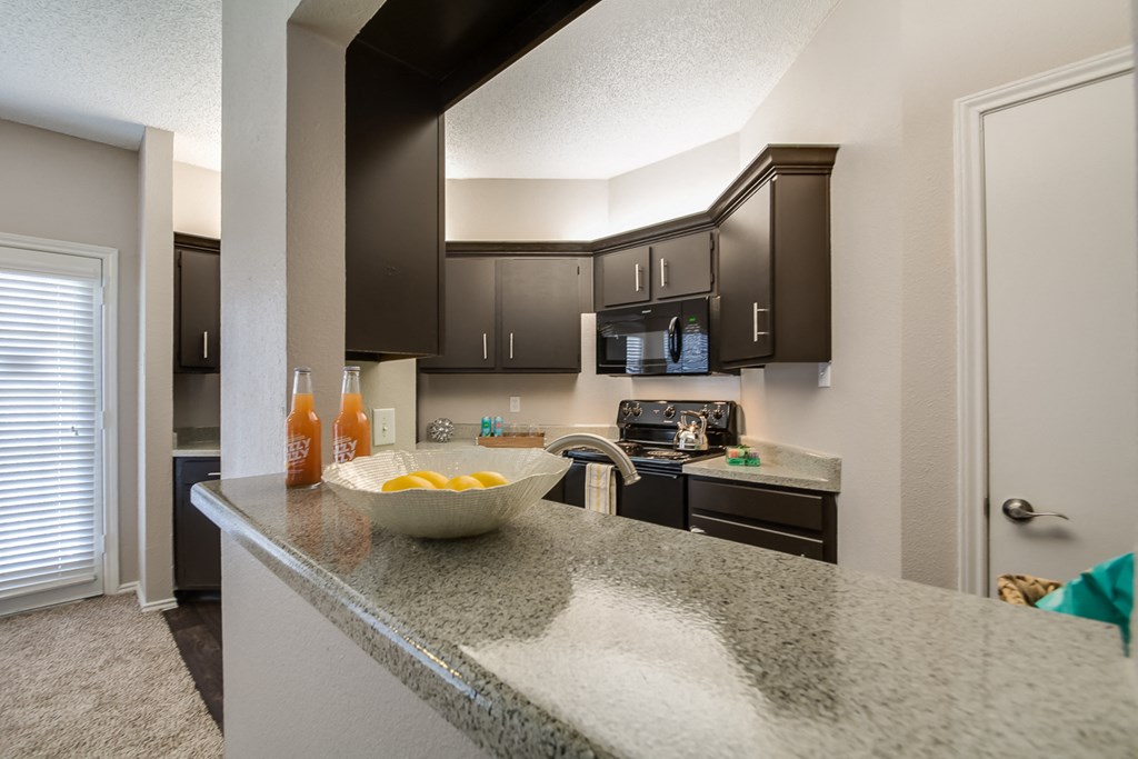 A kitchen with granite countertops and dark brown cabinets.