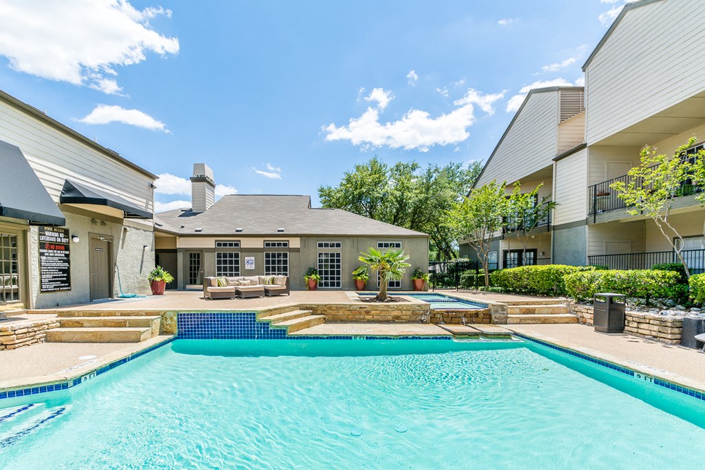 A swimming pool in front of a building with a blue sky and clouds in the background.