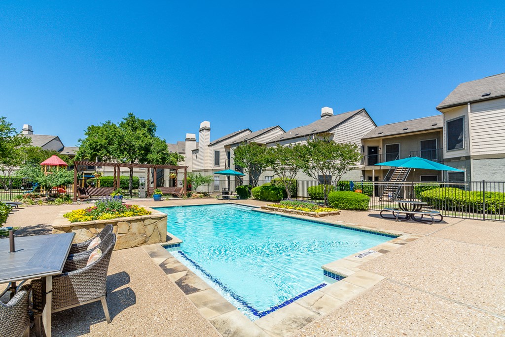 A pool surrounded by a patio with chairs and a table.