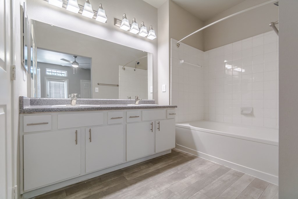 a bathroom with white cabinets and a tub and a sink and a mirror