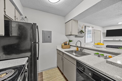 A black fridge stands in a kitchen with a white counter top.