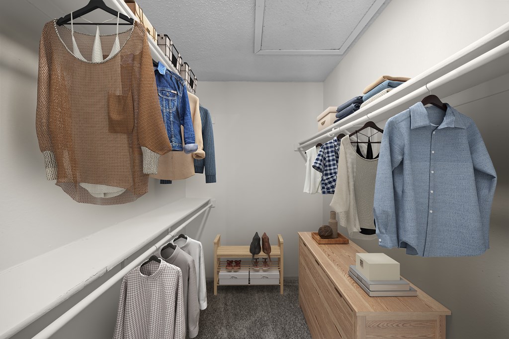 A walk in closet with clothes hanging and a bench underneath.