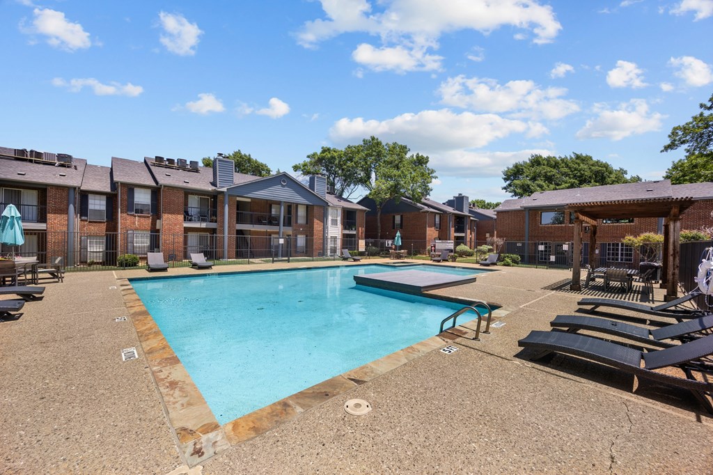 A swimming pool surrounded by sun loungers and apartment buildings.