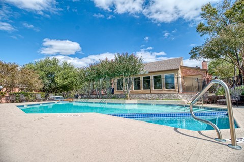 A swimming pool in front of a house with trees around.