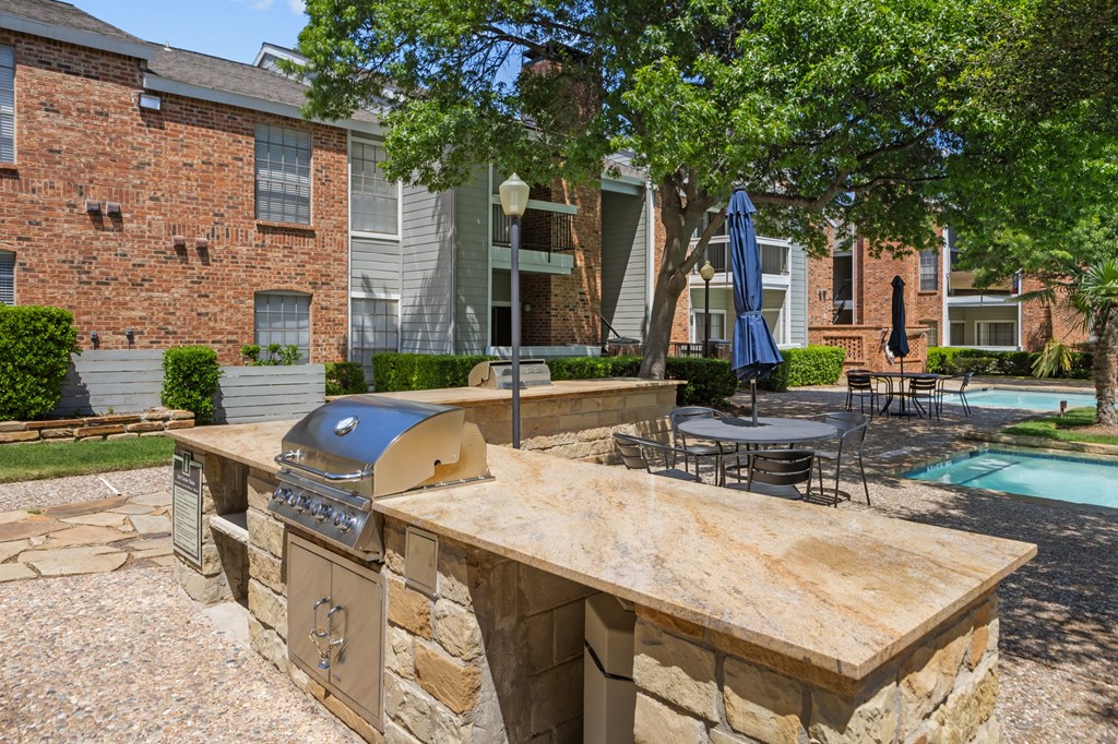 A stone barbecue grill is in the middle of a patio.
