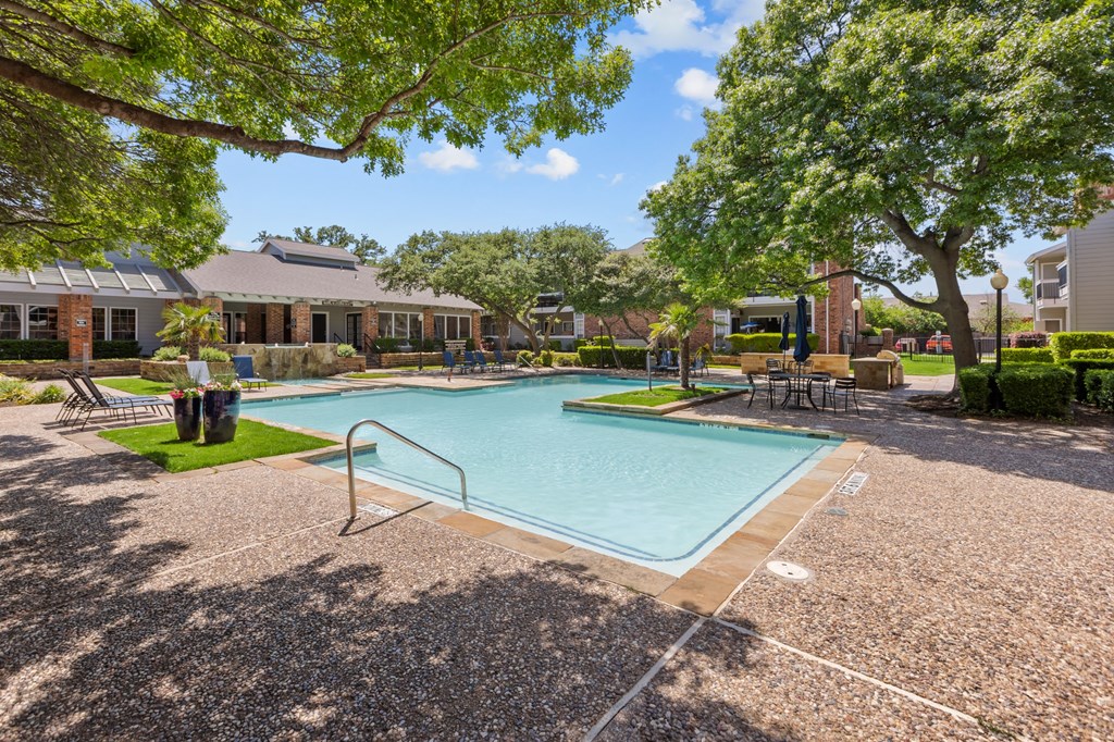 A small pool surrounded by a gravel area and trees.