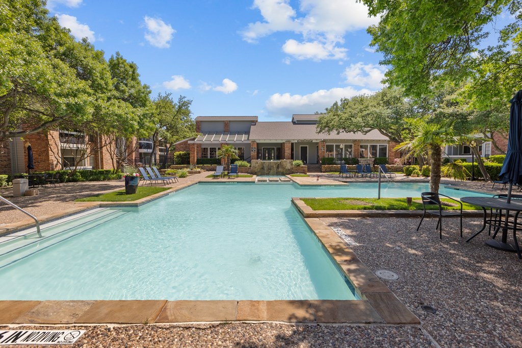 A large outdoor swimming pool surrounded by trees and a building in the background.