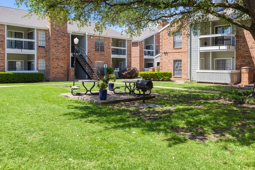 A grassy area in front of apartment buildings with a bench and picnic table.