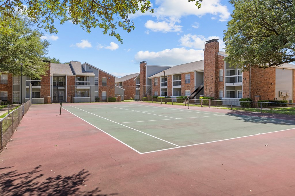A tennis court is surrounded by a brick building.