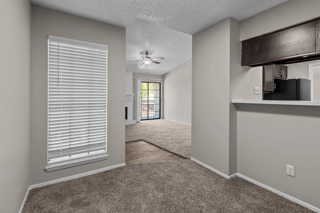 A room with a carpeted floor, a ceiling fan, and a window with blinds.