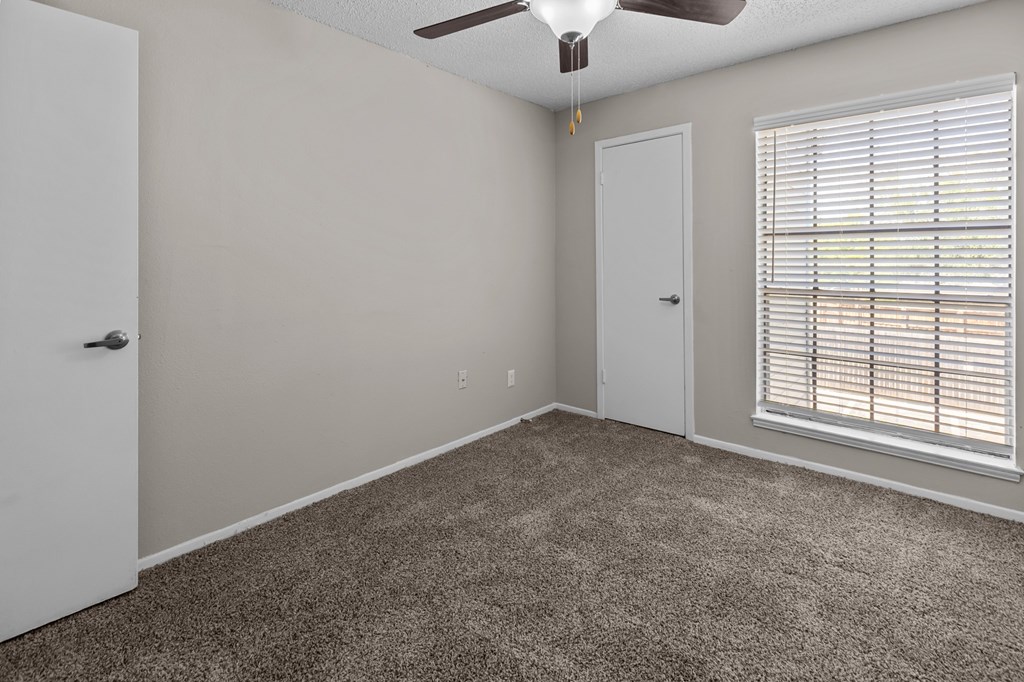 A room with a carpeted floor, a ceiling fan, and a window with blinds.