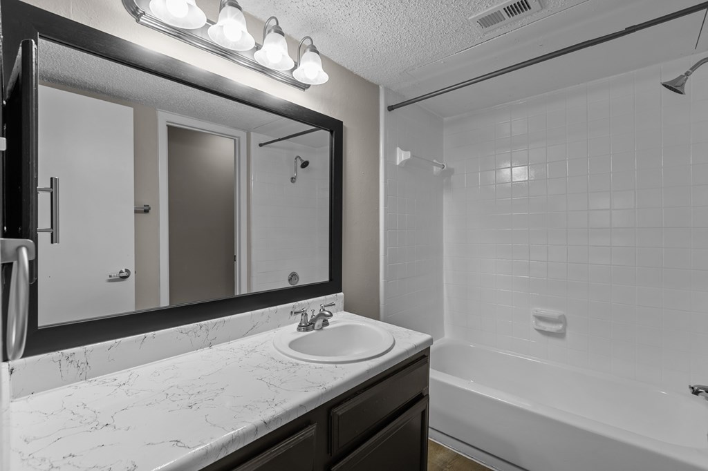 A bathroom with a marble countertop and a large mirror above the sink.