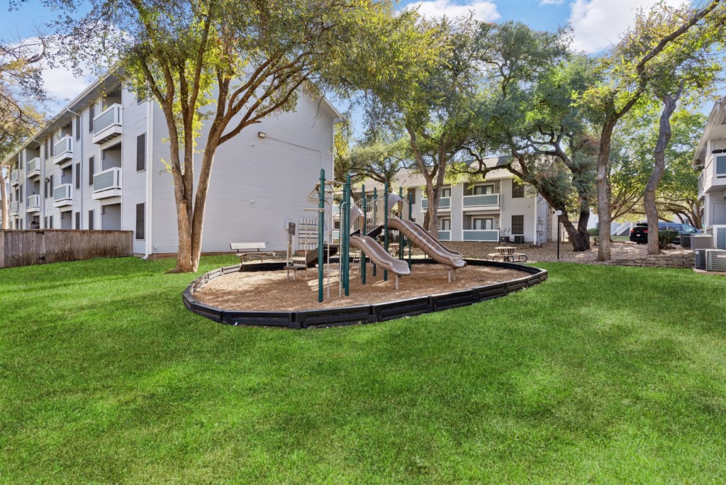 A playground with a slide and a green lawn in front of apartment buildings.