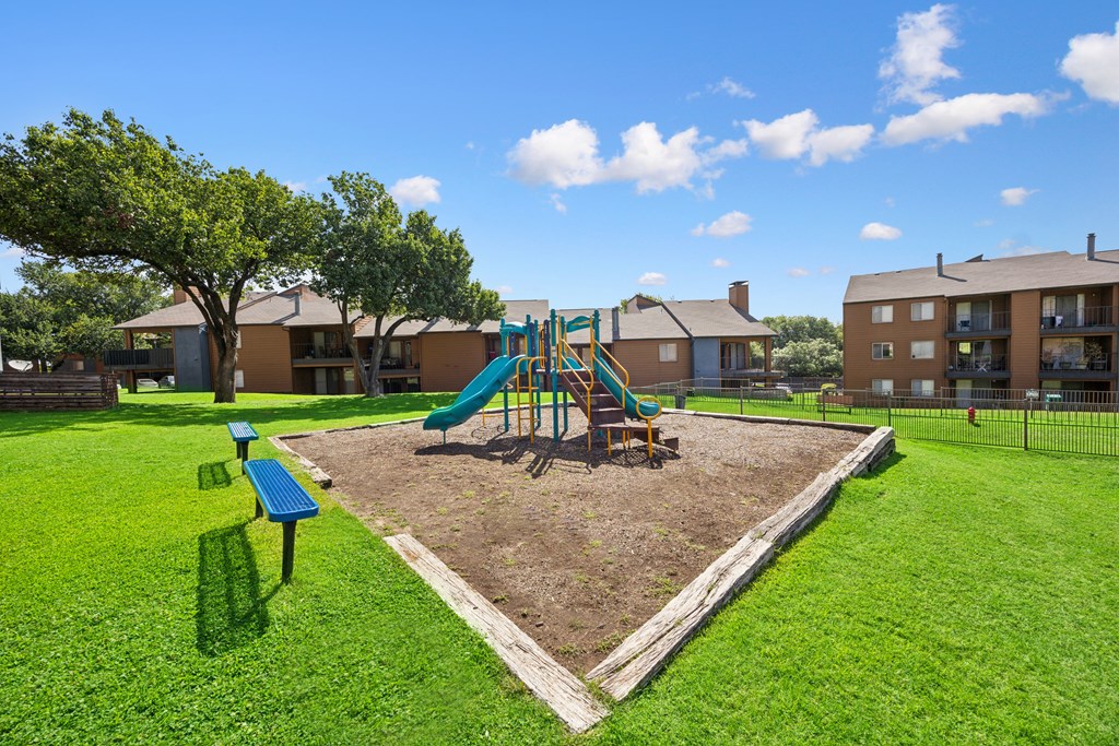 A playground with a green slide and a brown tree.