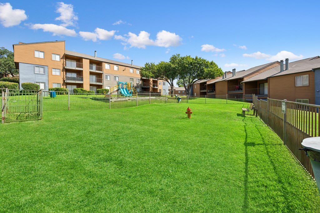 A large grassy area in front of apartment buildings with a playground and a fire hydrant.