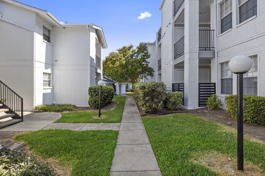a walkway between two apartment buildings with grass and trees