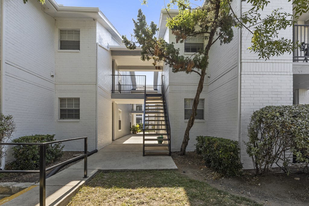 the entrance to a white apartment building with stairs and a tree