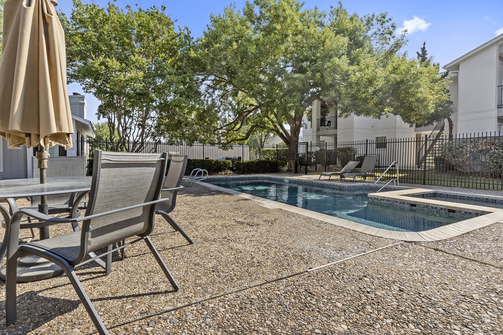 A pool surrounded by chairs and trees. at Tradewinds, Windcrest, Texas