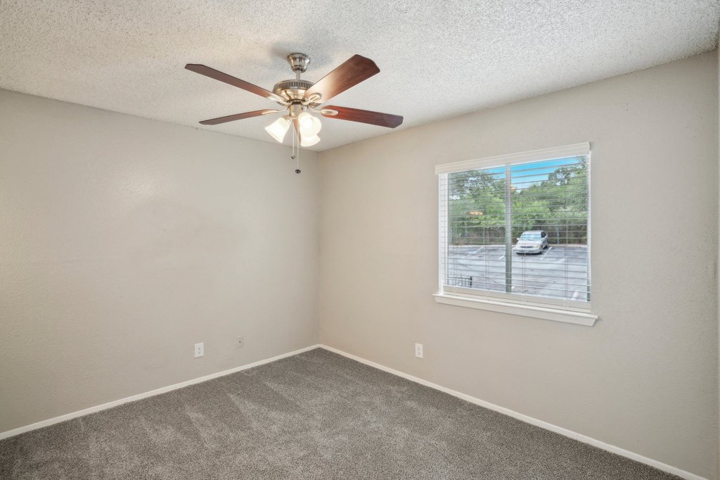 an empty bedroom with a ceiling fan and a window