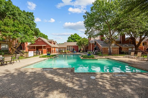 A large swimming pool surrounded by trees and a building in the background.