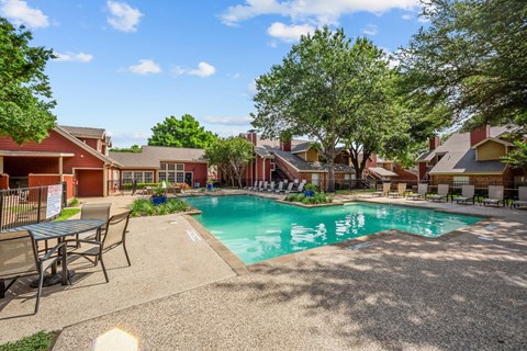 A pool surrounded by chairs and trees in a sunny day.