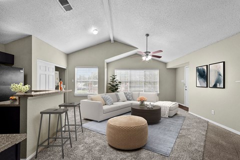 A living room with a white couch, a brown ottoman, and a ceiling fan.