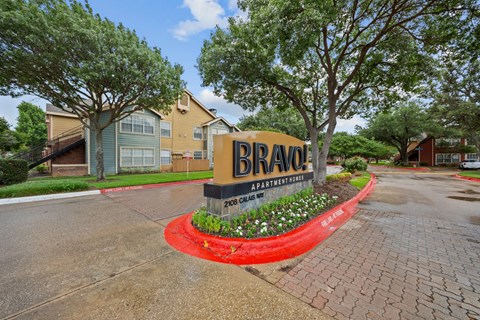 A sign for Bravo Apartments is in front of some trees and buildings.