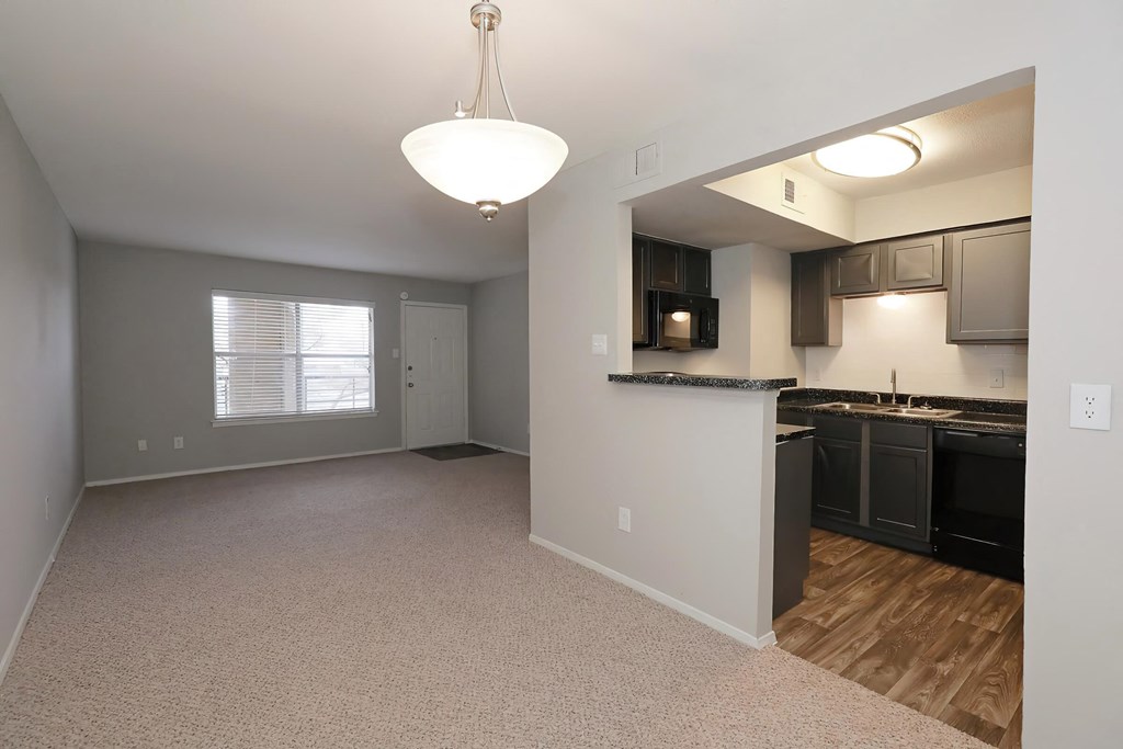 an empty living room with a kitchen in the background