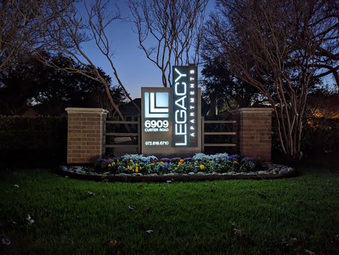 the sign for the legacy sign at night in front of a flower garden