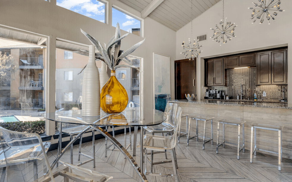 A yellow vase with a plant in it sits on a glass table.