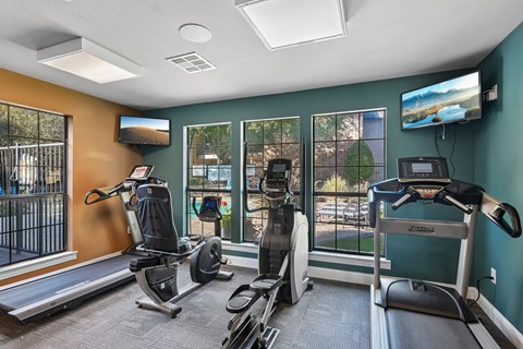 A gym with treadmills, exercise bikes, and a television.