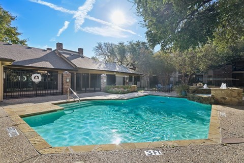 A swimming pool in front of a house with a sunny sky above.