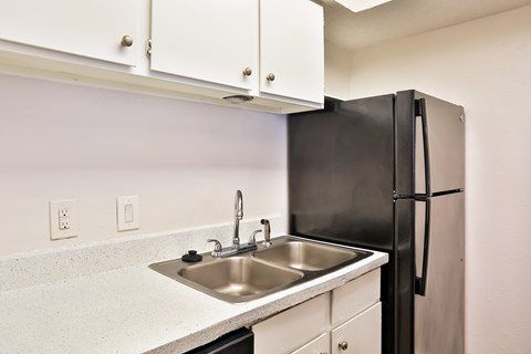 A kitchen with a black refrigerator and white cabinets.
