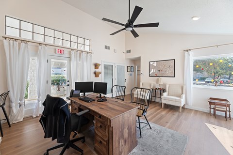 A room with a desk, chairs, and a ceiling fan.