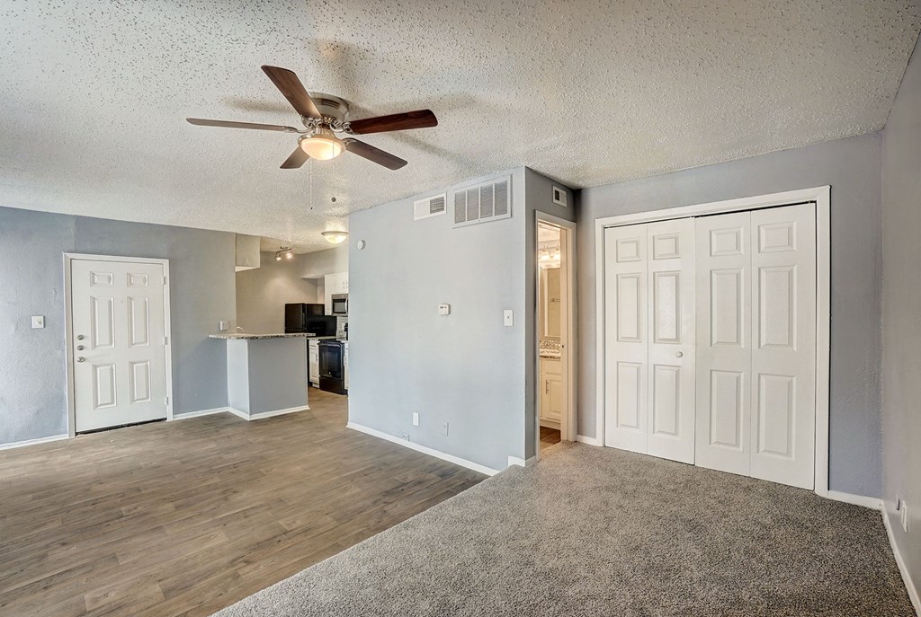 an empty living room with a ceiling fan and a kitchen