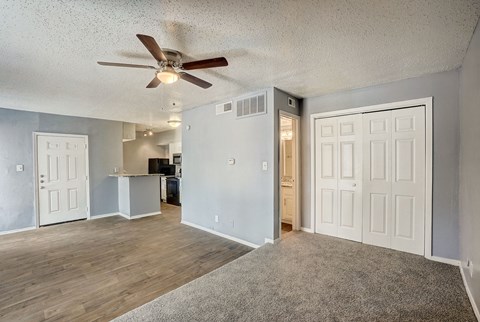 an empty living room with a ceiling fan and a kitchen