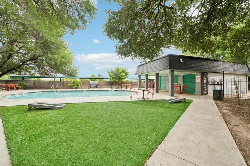 a pool with a pavilion and a grassy area with trees and a building