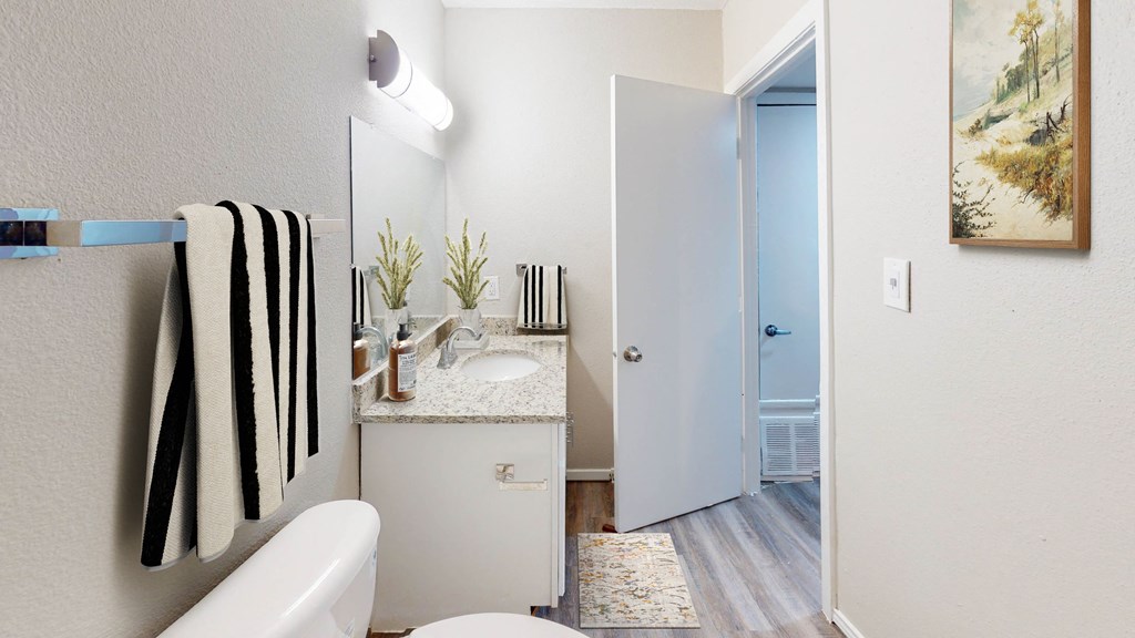 a bathroom with a white toilet and a white sink with a black and white towel hanging on at The Frederick, San Antonio Texas