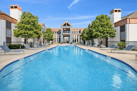 A large swimming pool in front of a building with trees on the side.