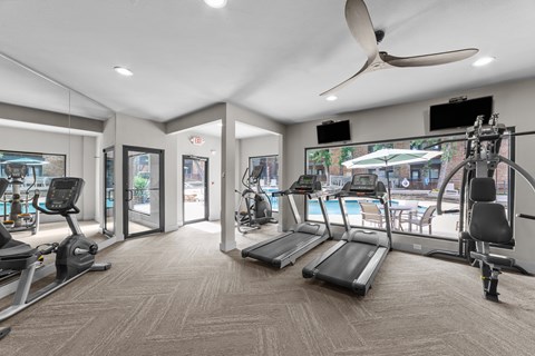 A spacious gym with treadmills, exercise bikes, and a fan.